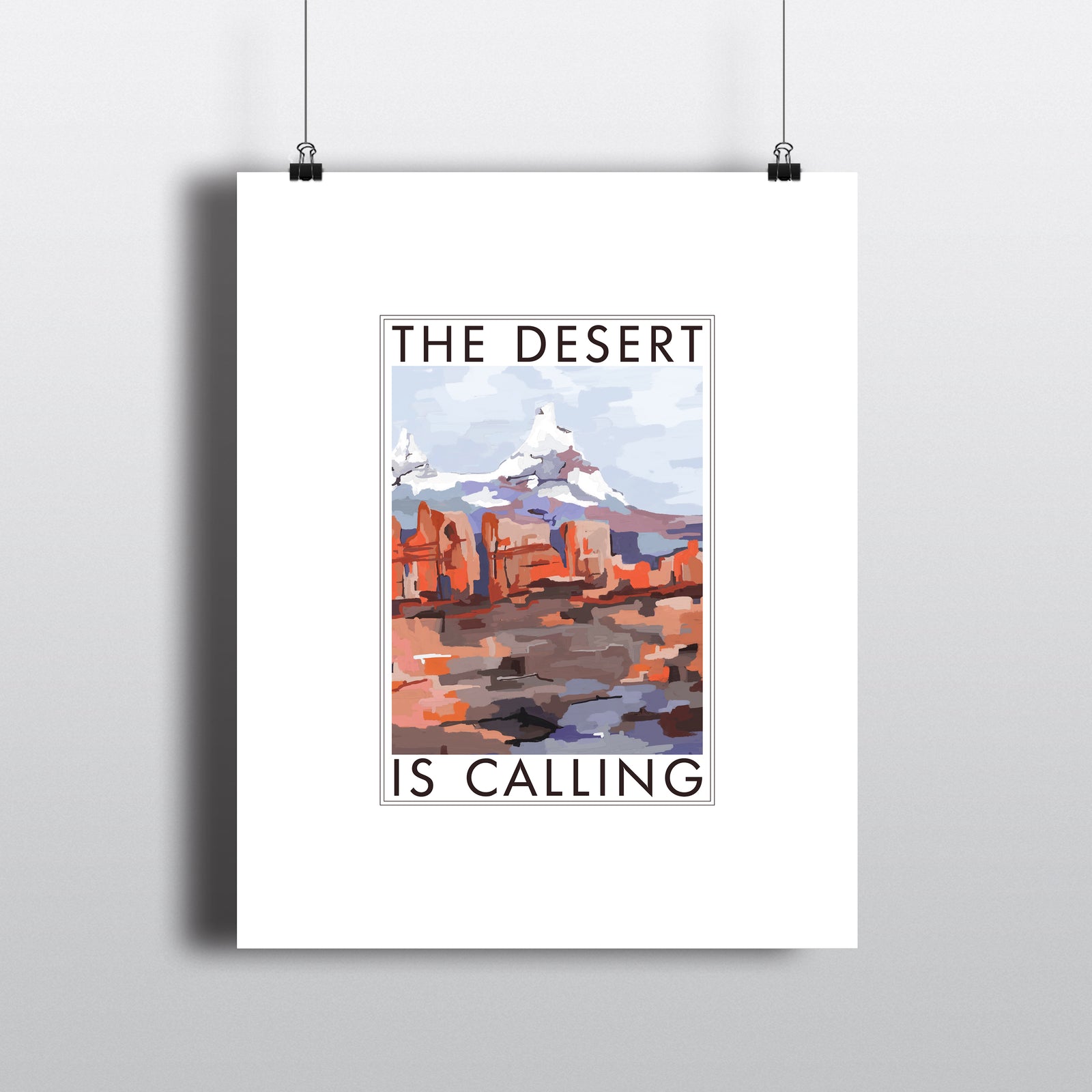 Art print with white border, THE DESERT IS CALLING text  framing abstract art of desert and mountain. Hanging by clips. 