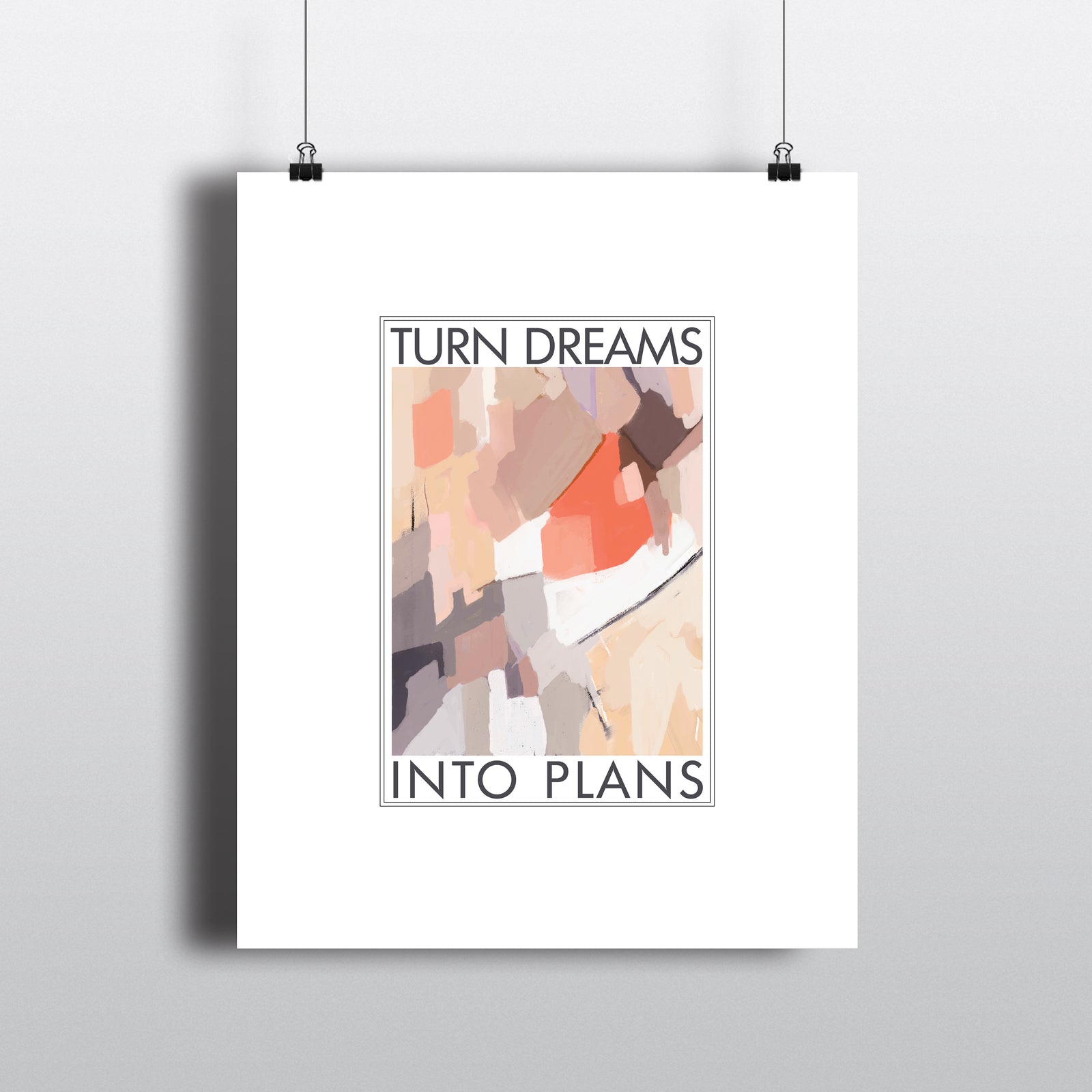 Art print with white border framing the text TURN DREAMS INTO PLANS and abstract art in shades of coral, tan lilac and mauve. Hanging by clips.